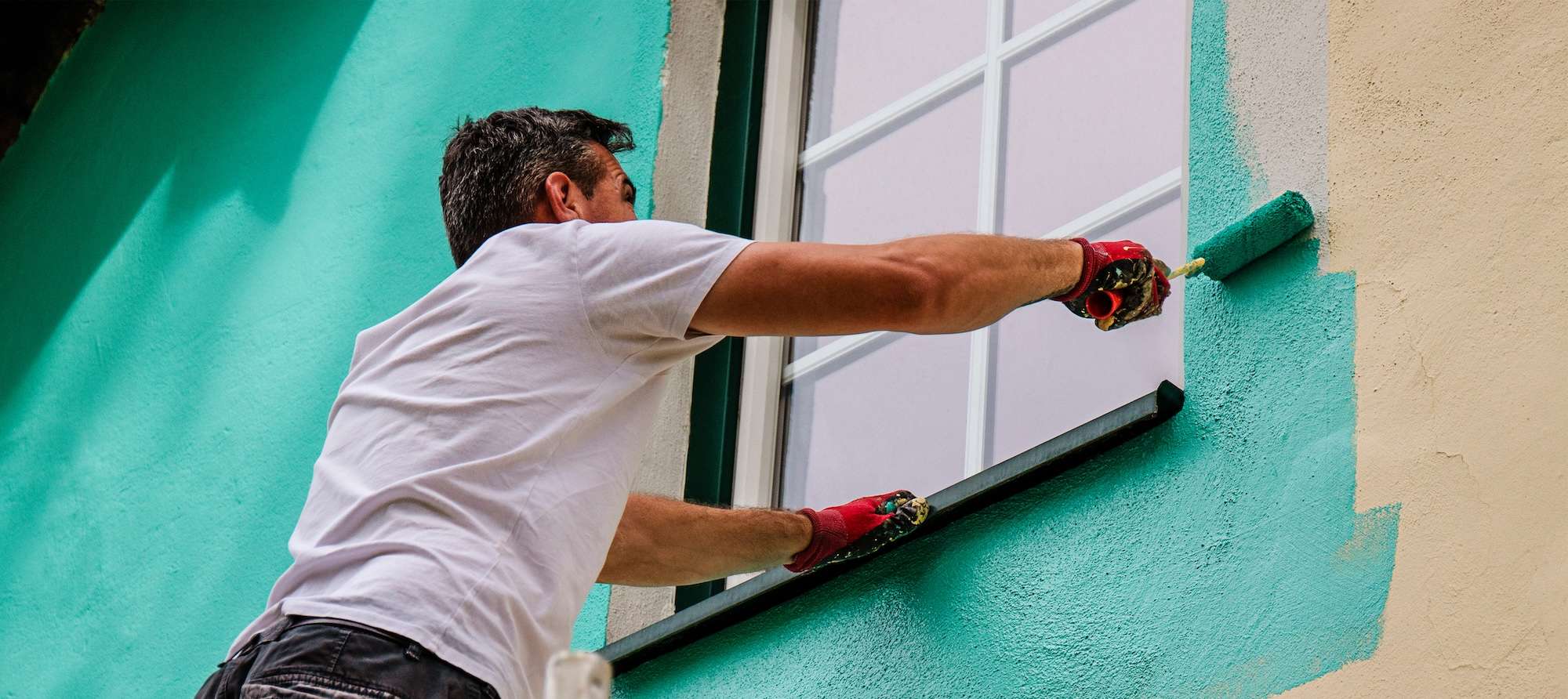 A worker paints the facade walls of a house with paint using a paint roller
