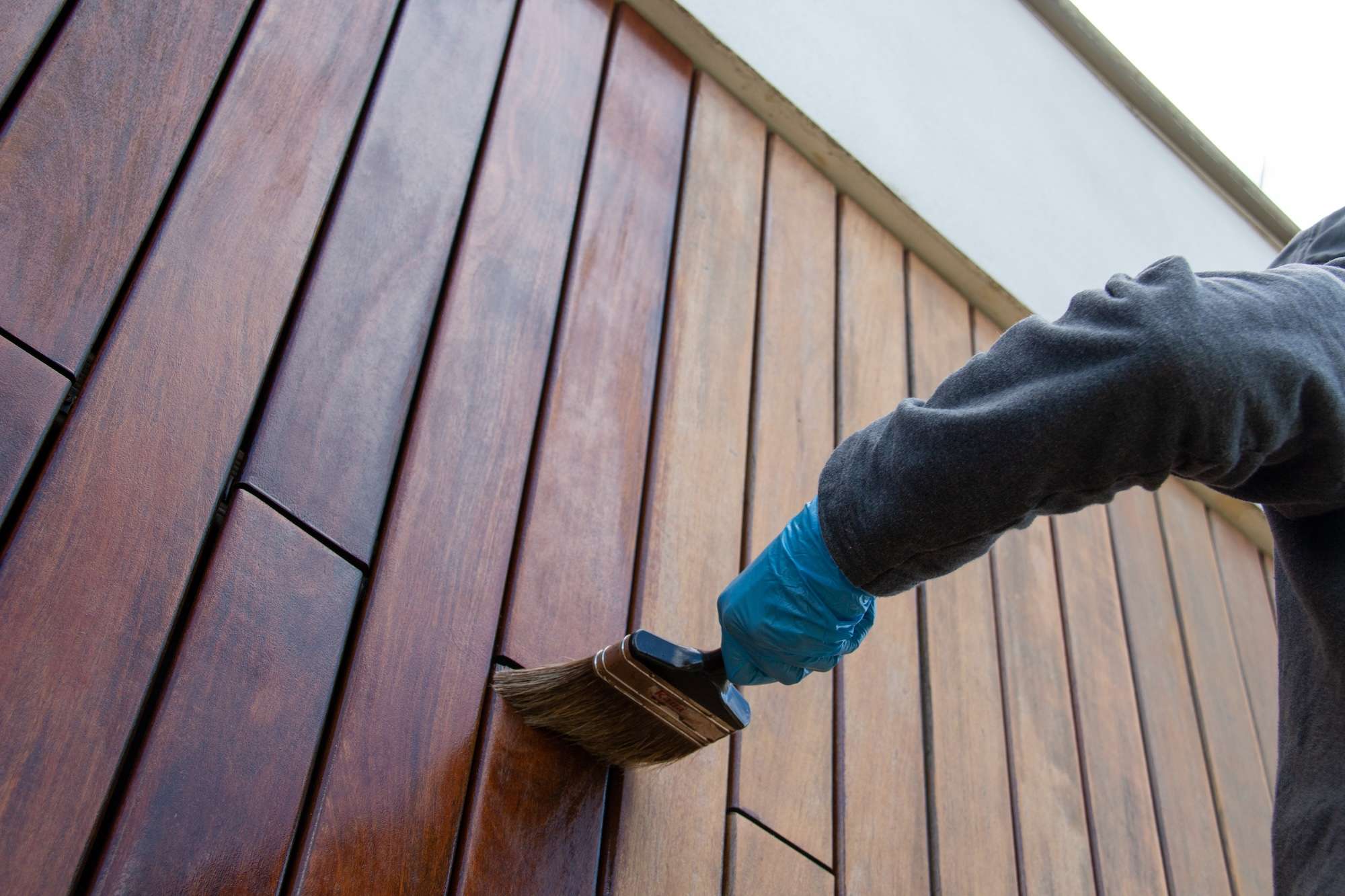 Painter with paintbrush painting house wood facade with protective oil, low angle perspective view